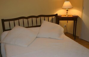 A neatly made bed with white linens and pillows, a wooden headboard, and a bedside table with a lamp.