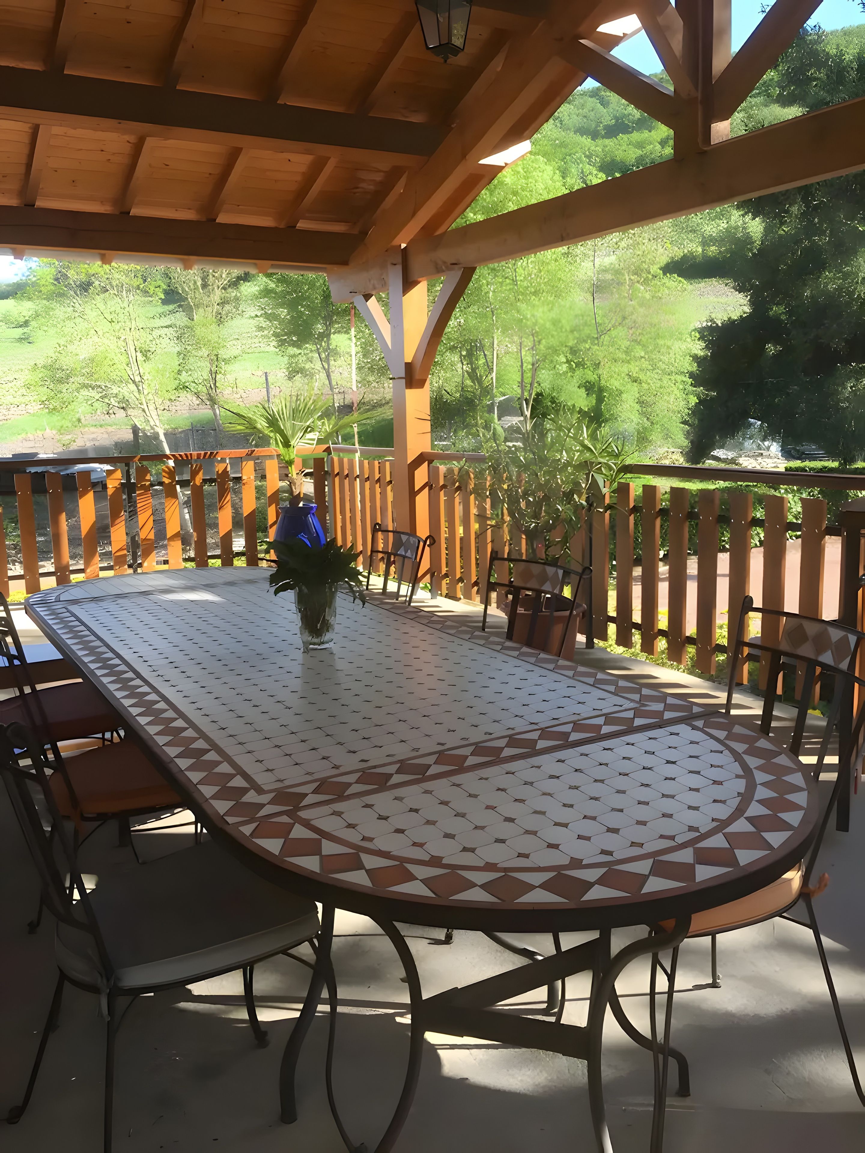 An outdoor patio with a round table and chairs, surrounded by a wooden fence and greenery.