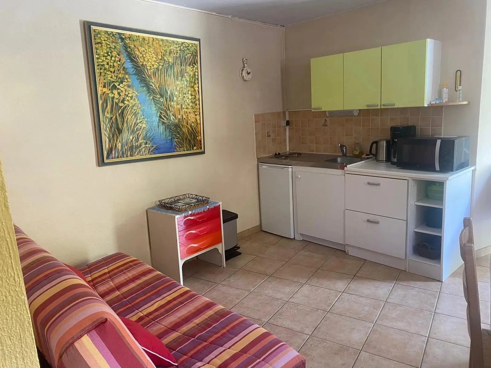 Un espacio habitable compacto con kitchenette, un sofá a rayas y un cuadro en la pared.