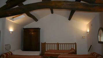 A room with a sloped ceiling, wooden beams, a bed with striped bedding, and wall-mounted lighting.