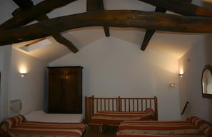 A room with a sloped ceiling, wooden beams, a bed with striped bedding, and wall-mounted lighting.