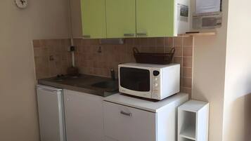 Cozinha compacta com micro-ondas, mini-geladeira e armários verdes.