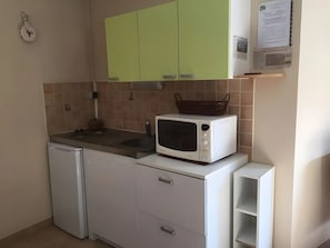 Una cucina compatta con forno a microonde, un piccolo frigorifero e mobili verdi.