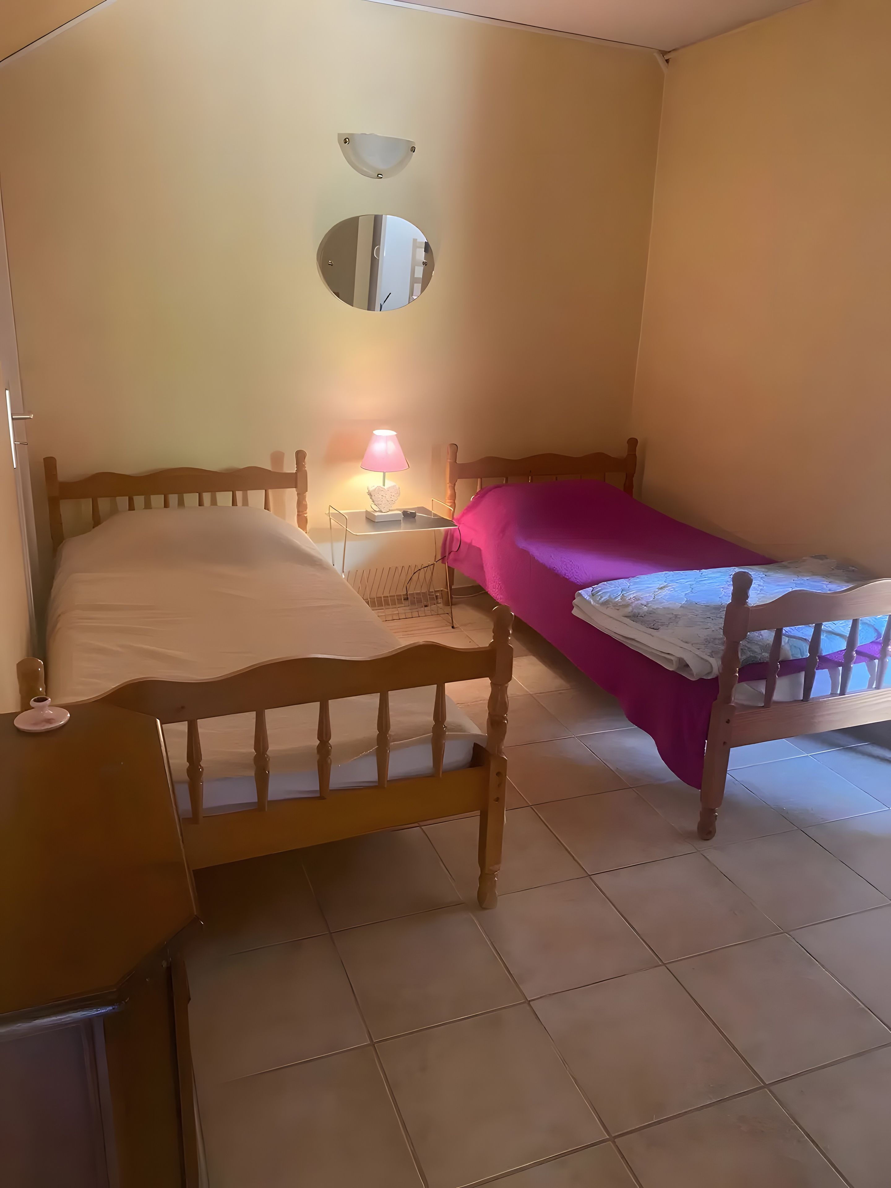 Ein Schlafzimmer mit zwei Holzbetten, einem Nachttisch mit Lampe und einem an der Wand befestigten Spiegel.