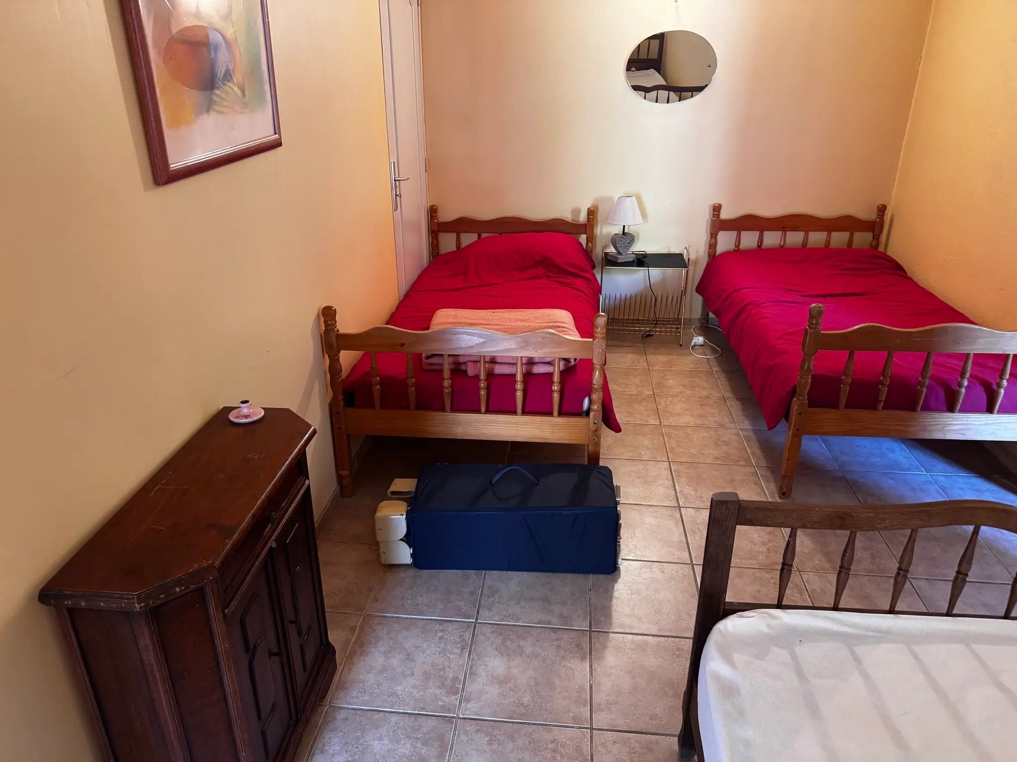 Una habitación pequeña con dos camas de madera, una mesita de noche, un espejo y un mueble auxiliar.