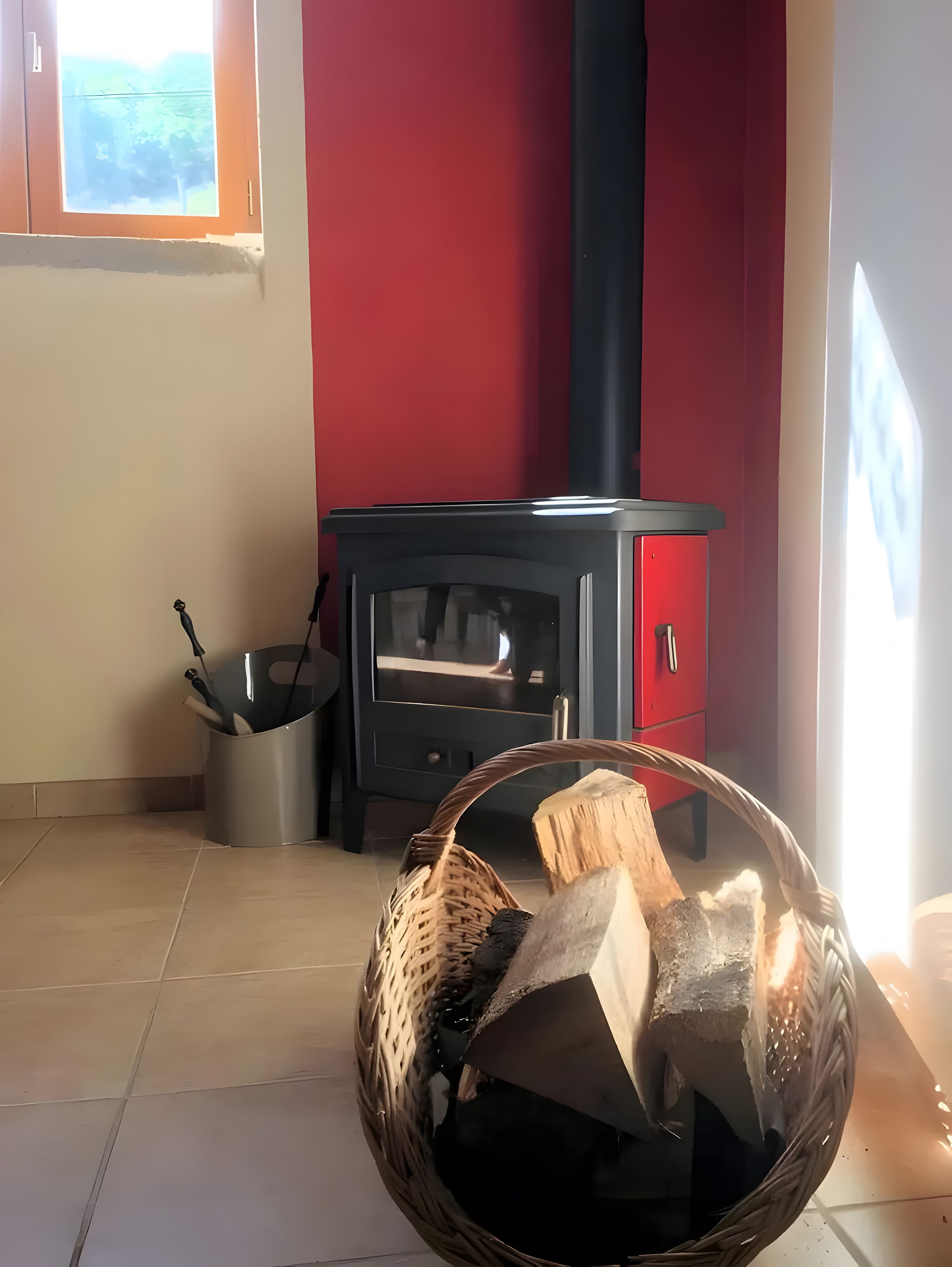 Una habitación con un estufa de leña negra, una pared roja y una ventana.