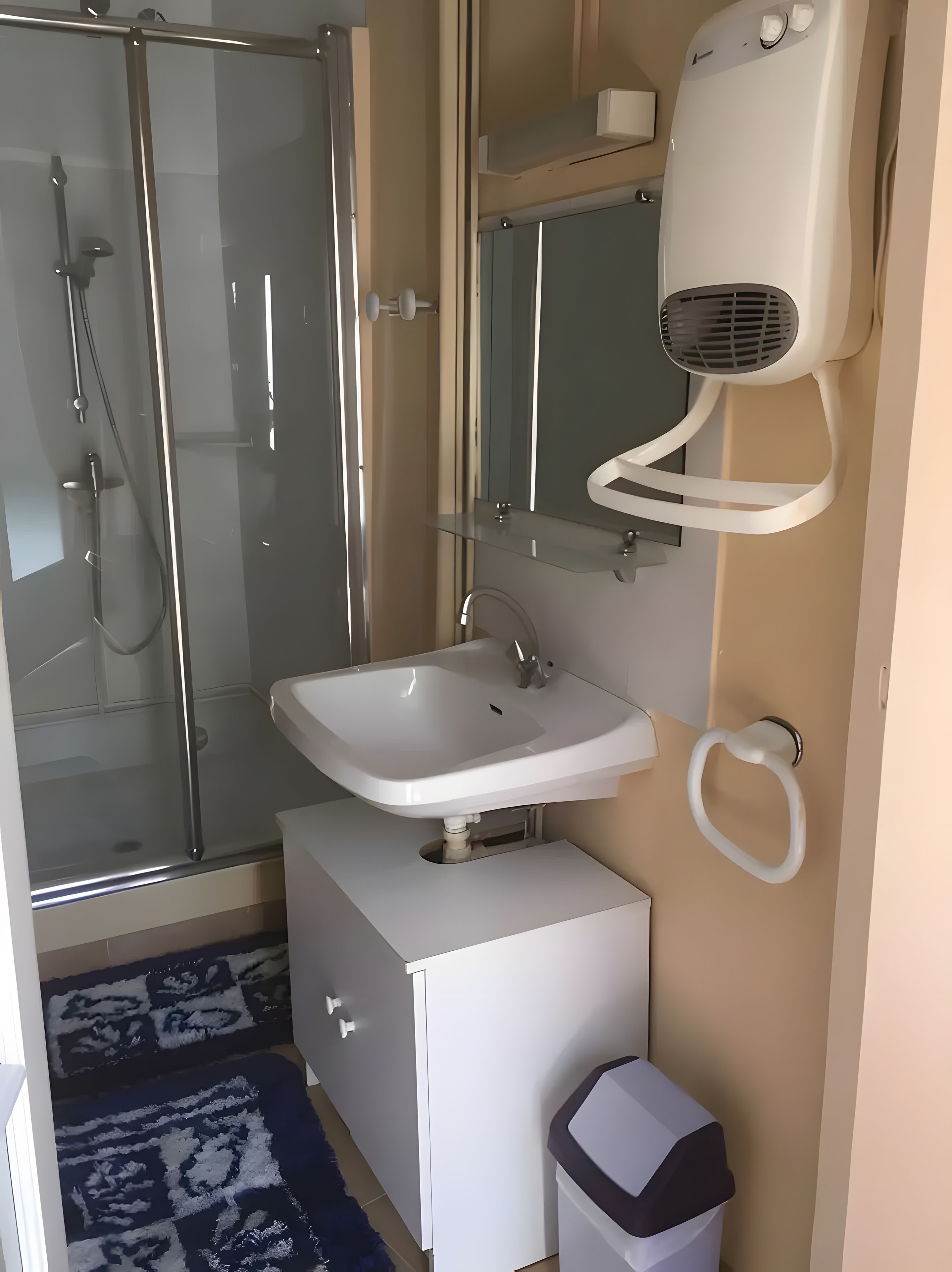 A bathroom with a glass shower enclosure, a white sink, a mirror, and a towel rack.