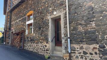 Un edificio de piedra con una puerta de madera y una ventana, un pequeño escalón que lleva a la entrada, y un cubo verde en el suelo.