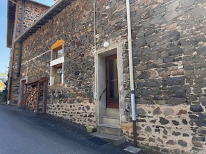Un edificio in pietra con una porta di legno e una finestra, un piccolo gradino che porta all'ingresso e un secchio verde a terra.