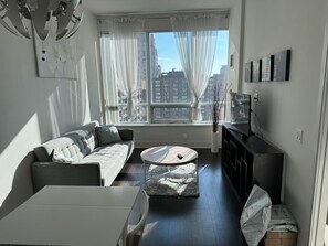 A modern living room with a sofa, coffee table, and a view of the cityscape through large windows. - Yorkville Upscale 1bed1bath | Pool | Gym (Toronto)