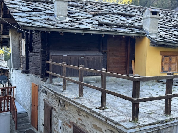Un edifici tradicional de fusta amb teulada de pedra, un balcó de fusta i una paret groga.