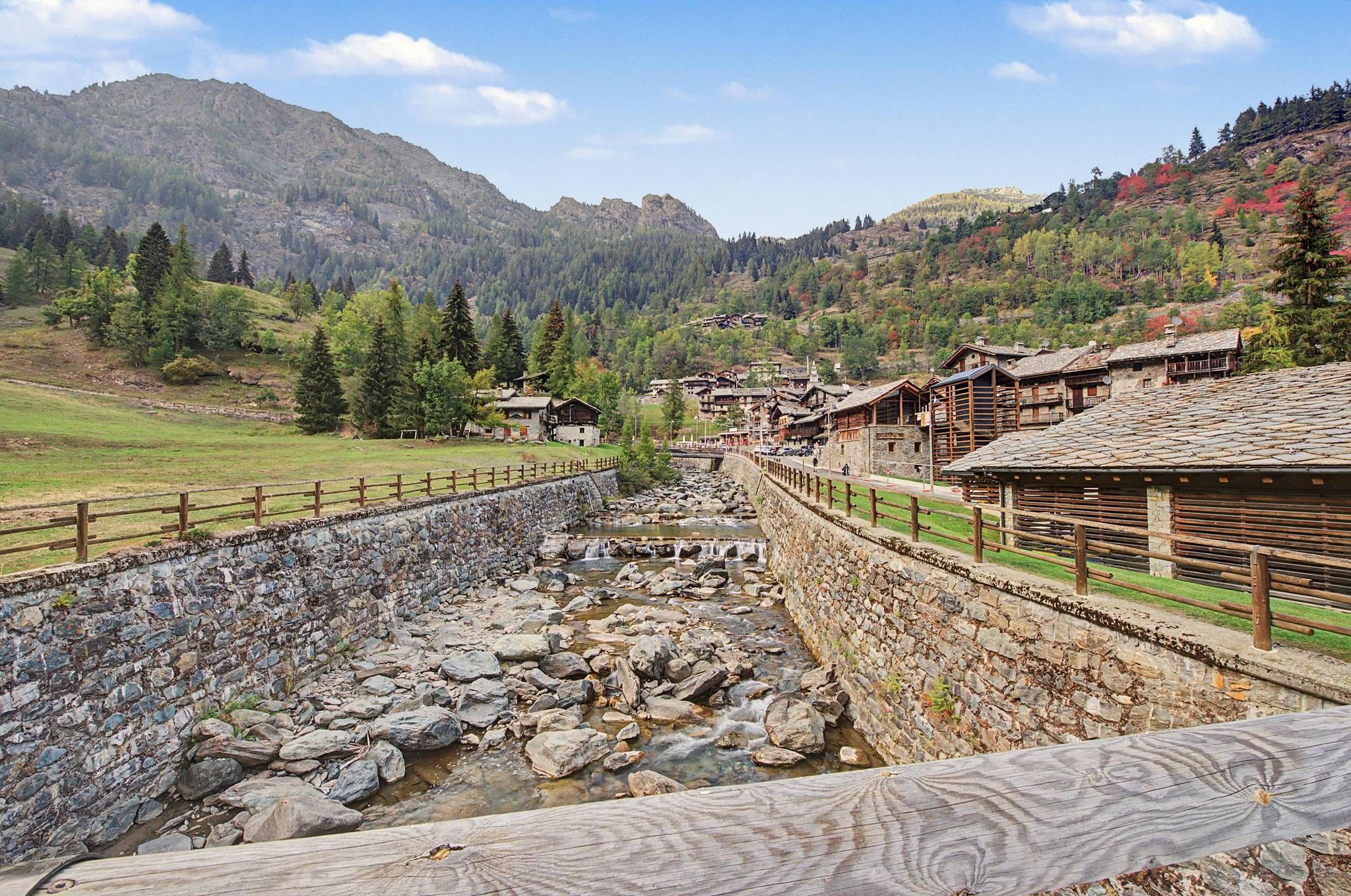 A stone-lined water channel with wooden buildings on one side and a mountainous backdrop.