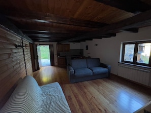 Ein Zimmer mit Holzboden, einer Couch, einem Fenster und Blick ins Freie.