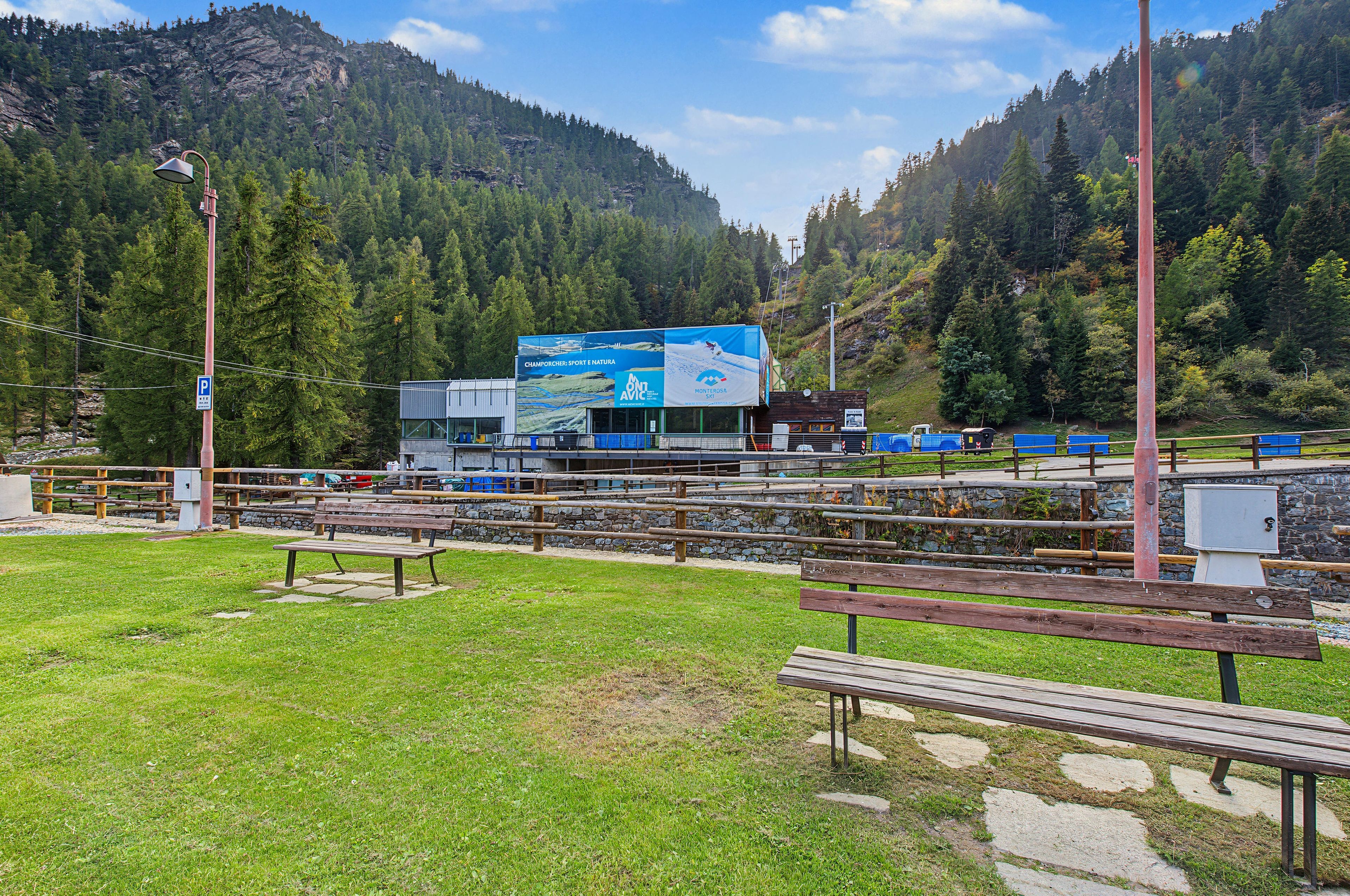 Eine gebirgige Landschaft mit einem Gebäude, das eine große blaue Werbung, Picknicktische und ein Parkschild zeigt.