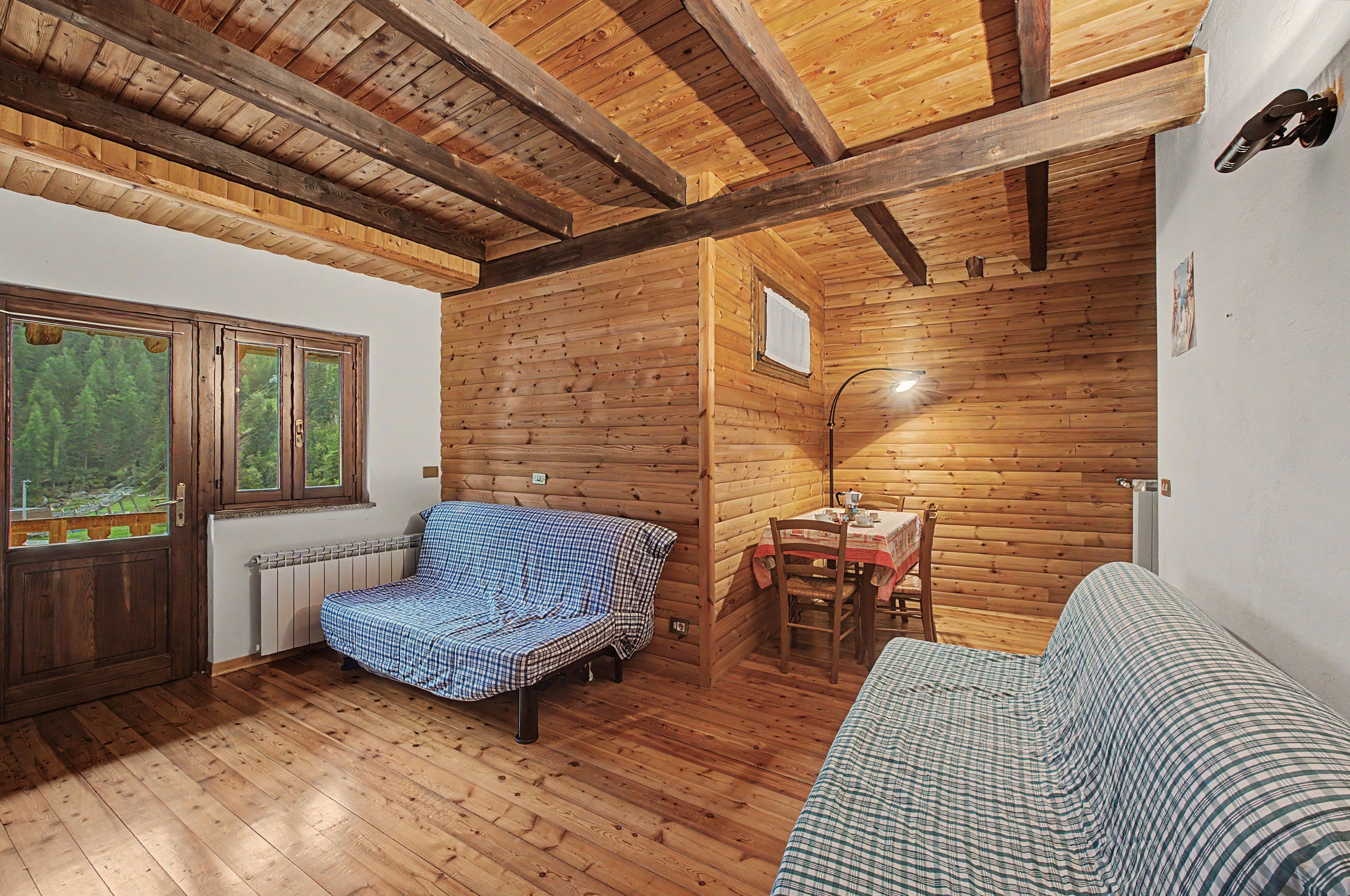 L’intérieur d’une cabane en rondins, avec un lit, une table entourée de chaises et une fenêtre donnant sur la forêt.