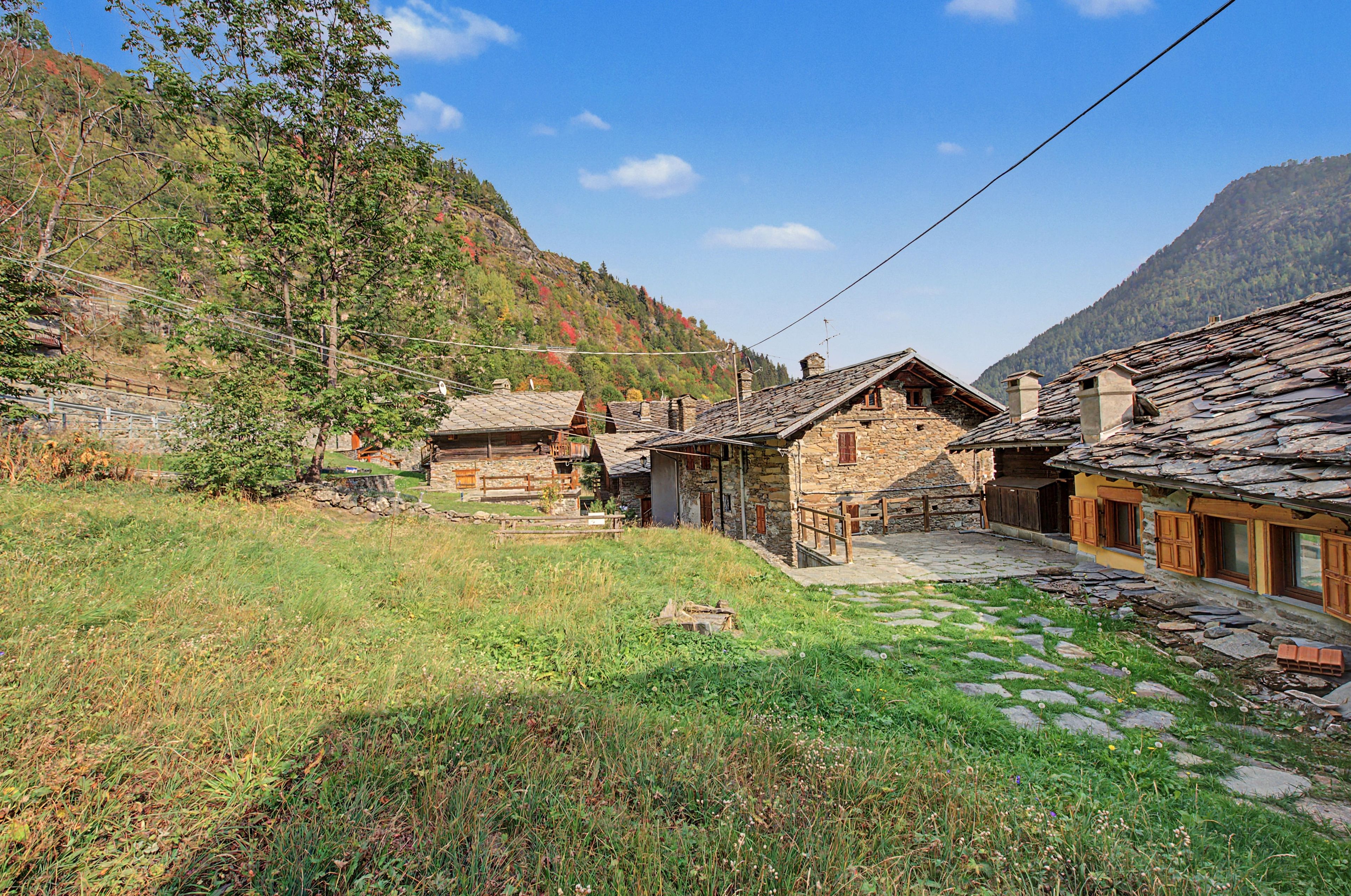 A traditional stone building with a sloped roof, surrounded by a stone wall and a grassy area with a clear sky above.