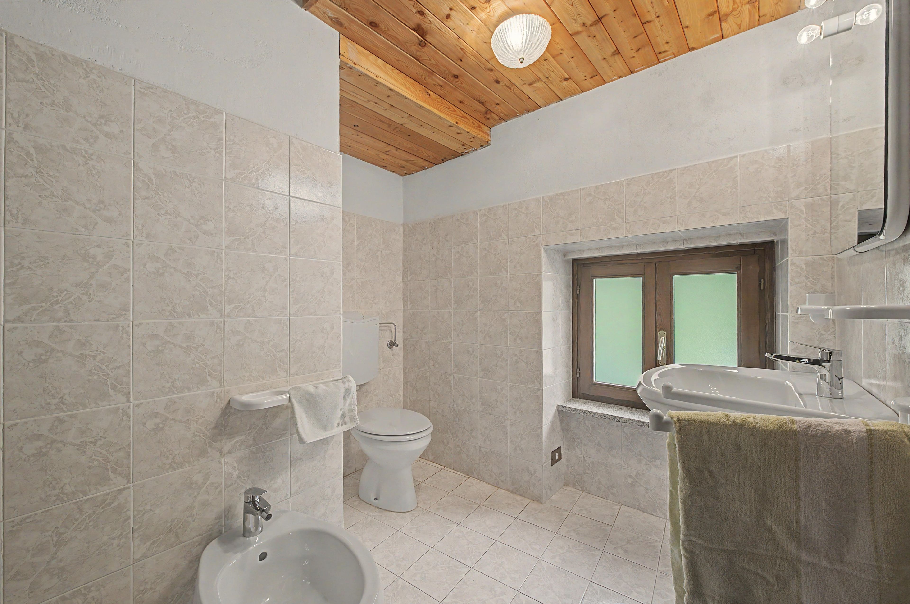 Un baño con inodoro, bidé, lavamanos y ventana.
