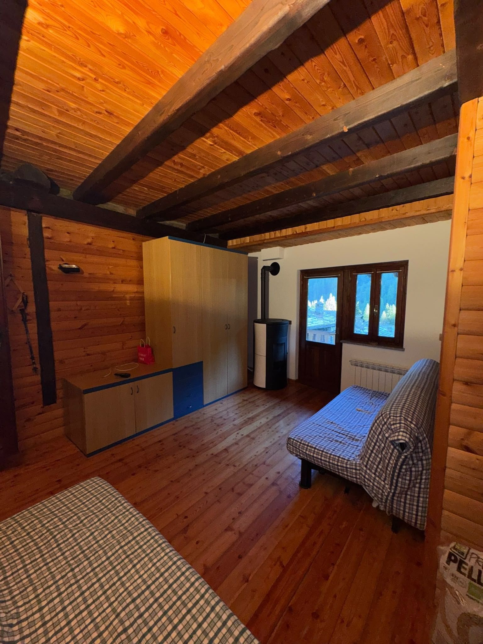 A cabin interior with a wooden ceiling, a sofa, a small table, and a window with a view of trees.
