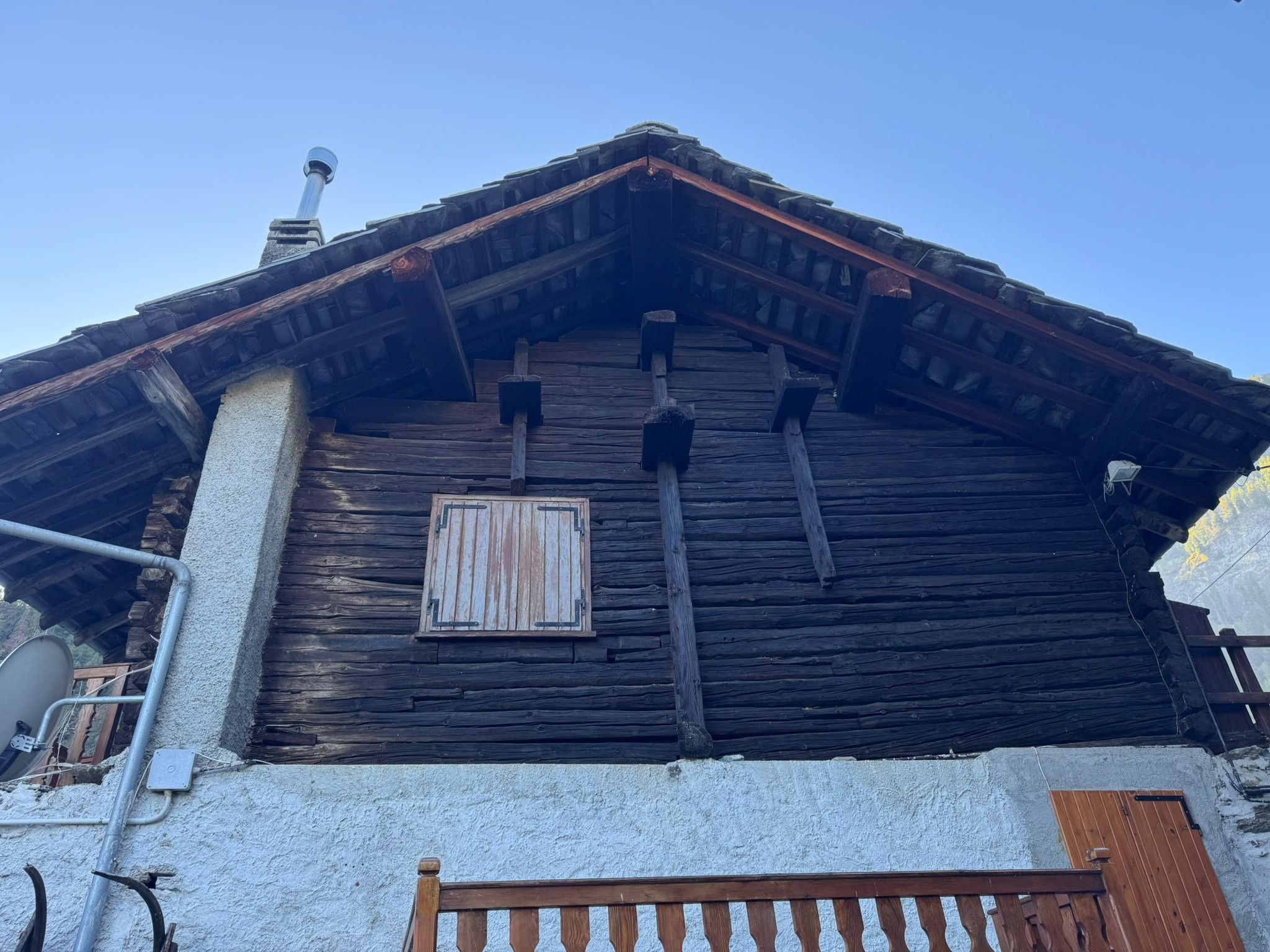 Eine rustikale Holzhütte mit geneigtem Dach, Schornstein und einem Fenster mit Fensterläden.