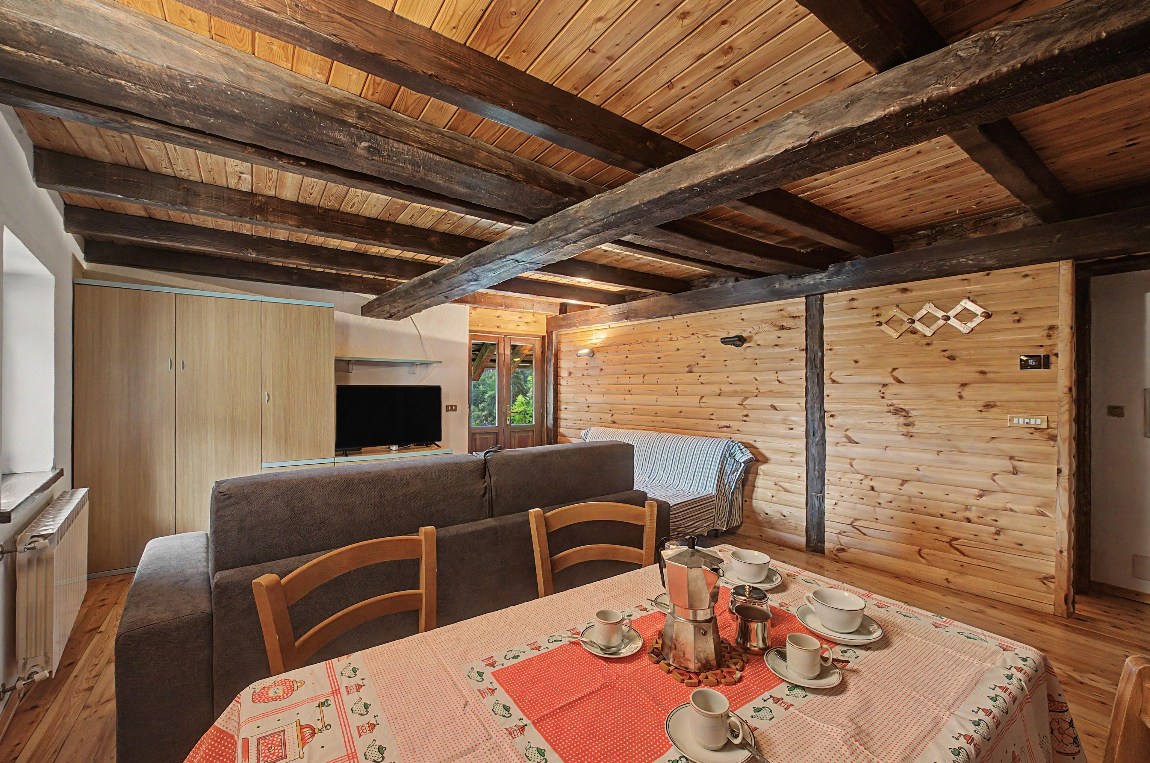 A cozy dining area with a wooden table set for four, a sofa, and a television in the background.