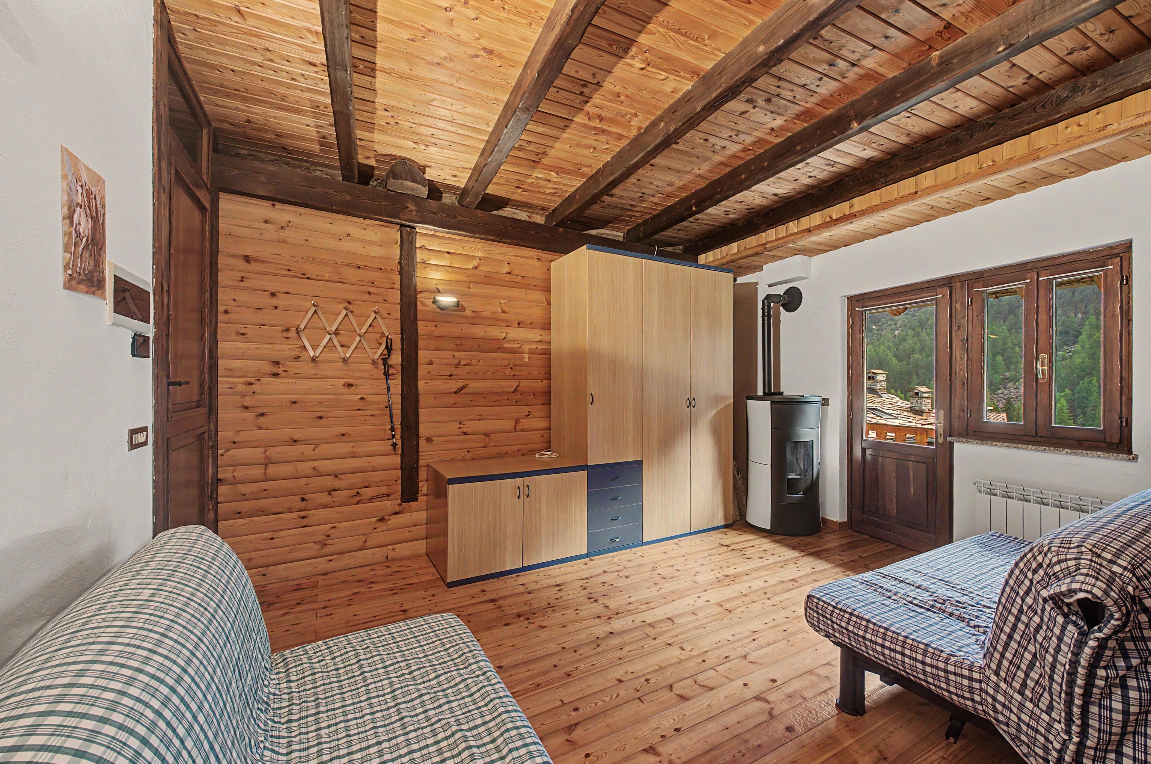 L’intérieur d’une cabane avec des murs et un plafond en bois, un lit, un canapé, une petite kitchenette et une fenêtre donnant sur les arbres.