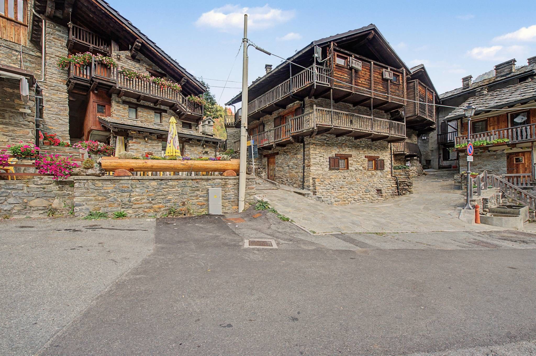 Un bâtiment traditionnel en pierre, doté de balcons en bois et de jardinières fleuries, une rue pavée et un ciel dégagé.