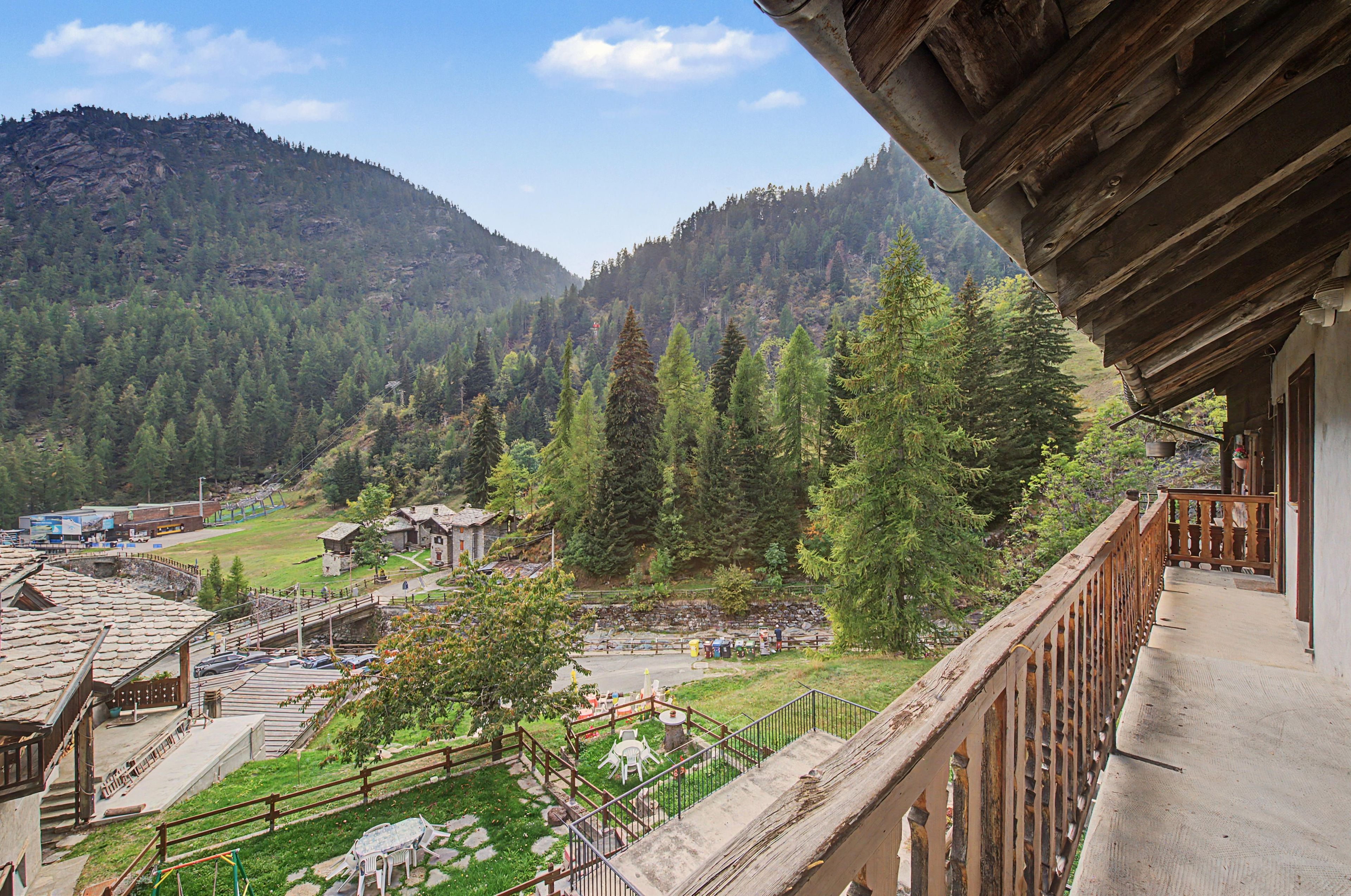 A mountain view with a wooden balcony overlooking a village with traditional buildings and a clear sky.
