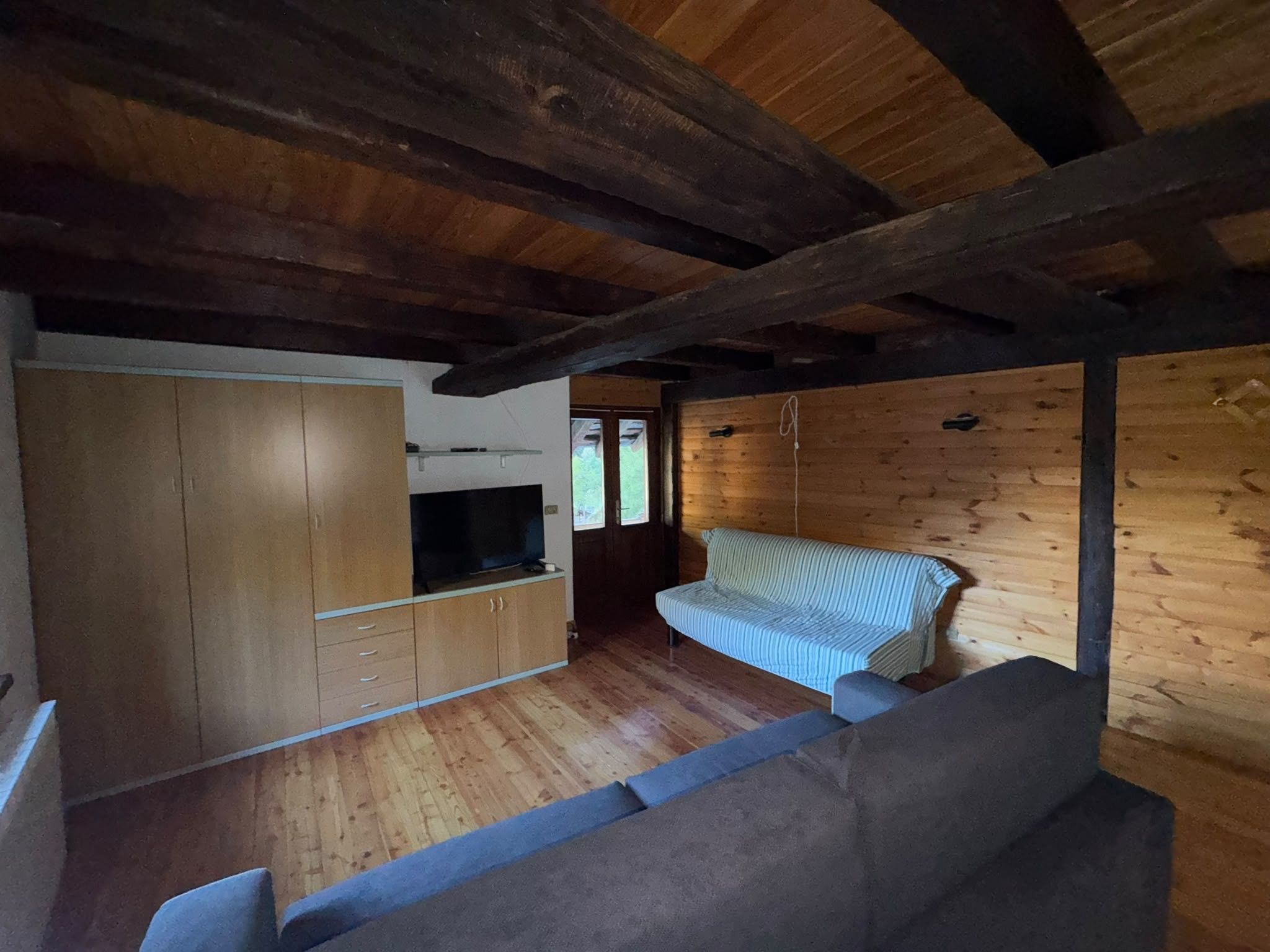 A compact room with a wooden ceiling, a sofa, a television, and a wooden wardrobe.