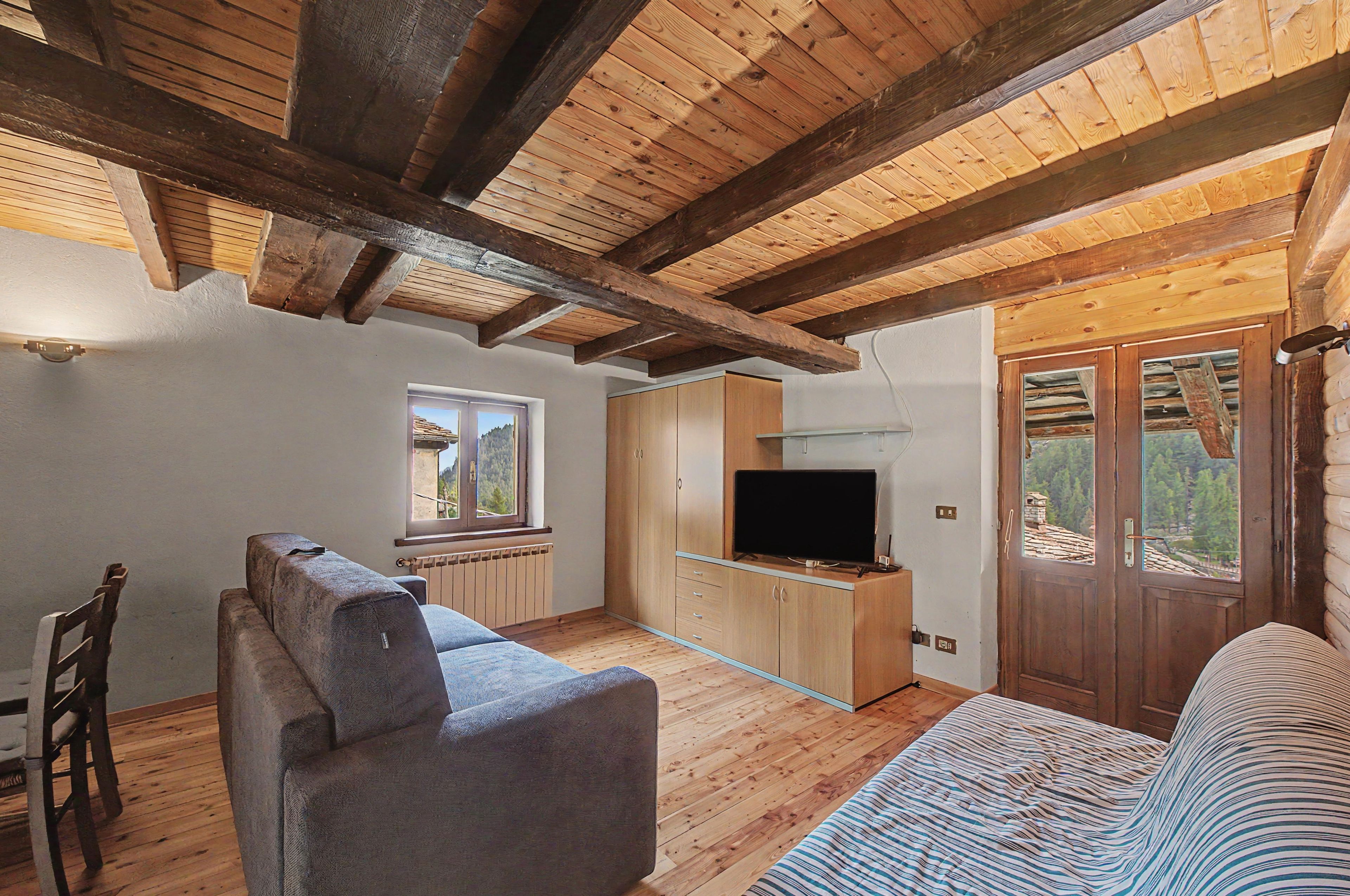 Ein gemütliches Wohnzimmer mit einer Couch, einem Fernseher und einem Fenster mit Blick ins Freie.