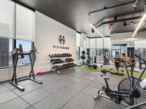 Ein Fitnessraum mit Trainingsgeräten, einem an der Wand befestigten Hantelständer und Blick auf die Stadt.