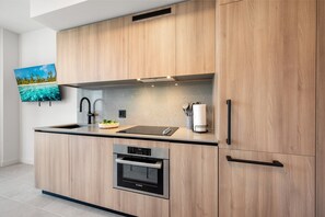 Eine moderne Küche mit Holzschränken, einem Bosch-Backofen, einer Spüle und einem an der Wand montierten Flachbildfernseher.