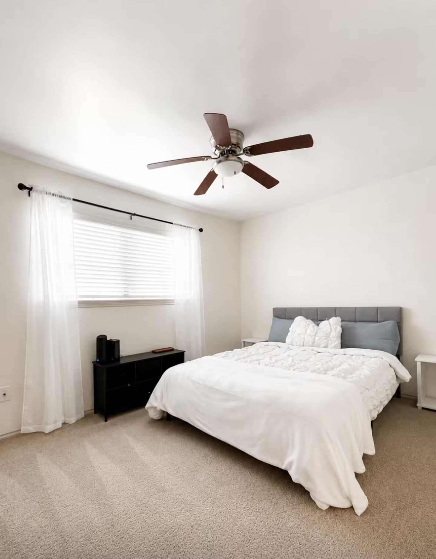 A bedroom with a bed, a ceiling fan, a window with blinds, a bedside table, and a nightstand.