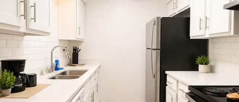A modern kitchen with white cabinetry, a black refrigerator, a stove, and a sink.