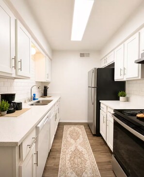 A modern kitchen with white cabinetry, a black refrigerator, a stove, and a sink. - Ashton - Relax & Recharge - Cozy 2BR Retreat (Waxahachie)