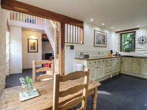 A spacious kitchen with a wooden dining table, a staircase, and a view of the outdoors. - Pandy Farmhouse (Dolgellau)