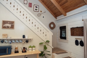 A kitchen with a wooden staircase, a coffee machine, tea and coffee containers, and a hanging plant. - Lucky Otter: Cozy + Artsy Lakeside Log Cabin (Mount Nebo)
