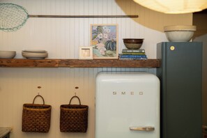 A kitchen with a white refrigerator, wooden shelves, a hanging net, and woven baskets. - Lucky Otter: Cozy + Artsy Lakeside Log Cabin (Mount Nebo)