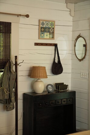 A room with a white wooden wall, a hanging lamp, a framed geometric artwork, a mirror, and a dark wooden console with drawers. - Lucky Otter: Cozy + Artsy Lakeside Log Cabin (Mount Nebo)