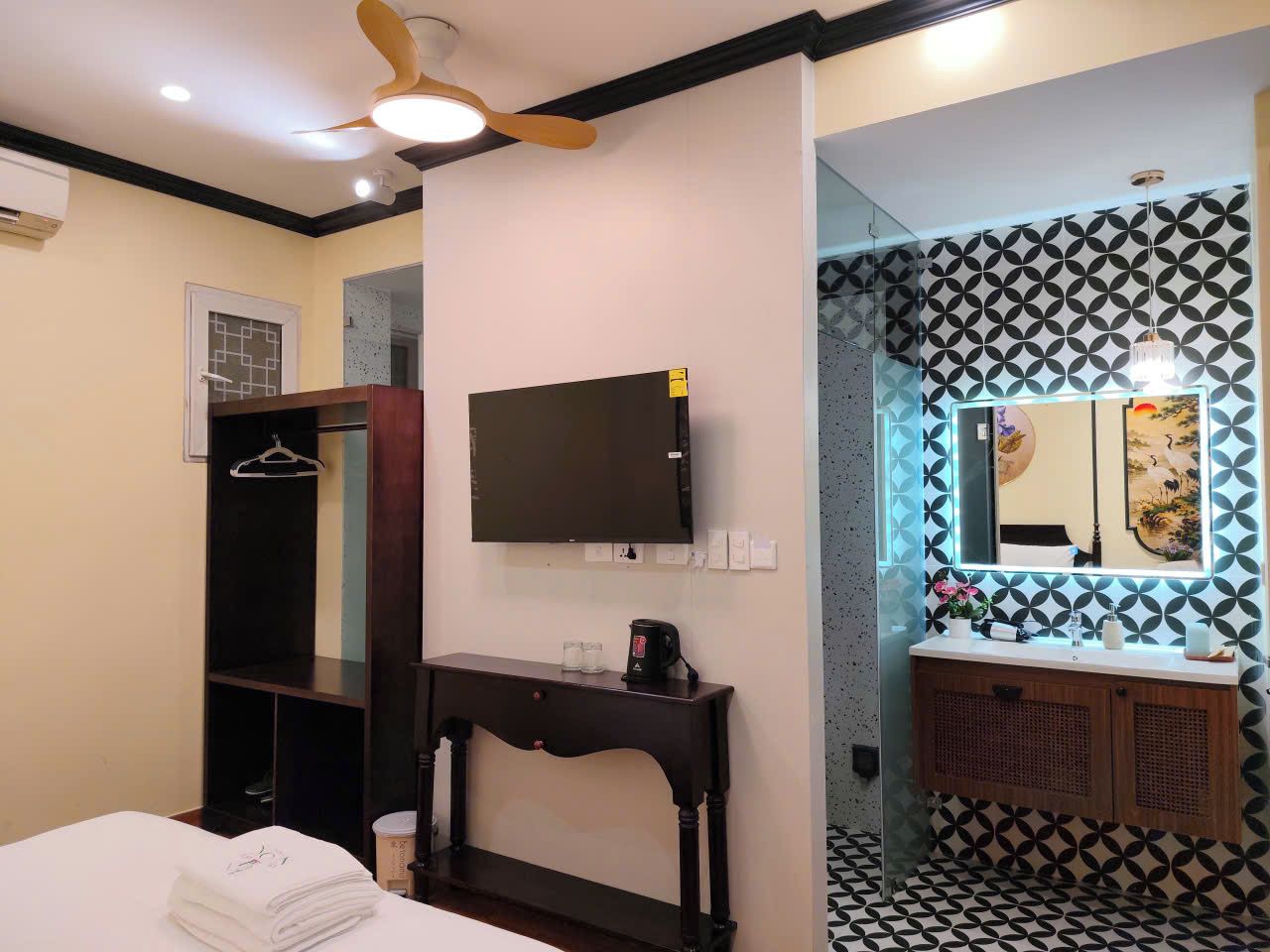 Una habitación de hotel con cama, escritorio con cafetera, televisión, armario y baño con salpicadero de azulejos estampados y espejo.