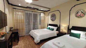 Une chambre d’hôtel avec deux lits, un bureau, une chaise, un ventilateur de plafond et une fenêtre avec des rideaux.