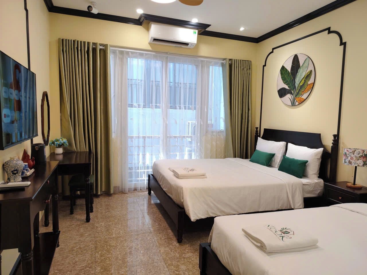 A hotel room with two beds, a desk, a chair, a TV, and a window with curtains.