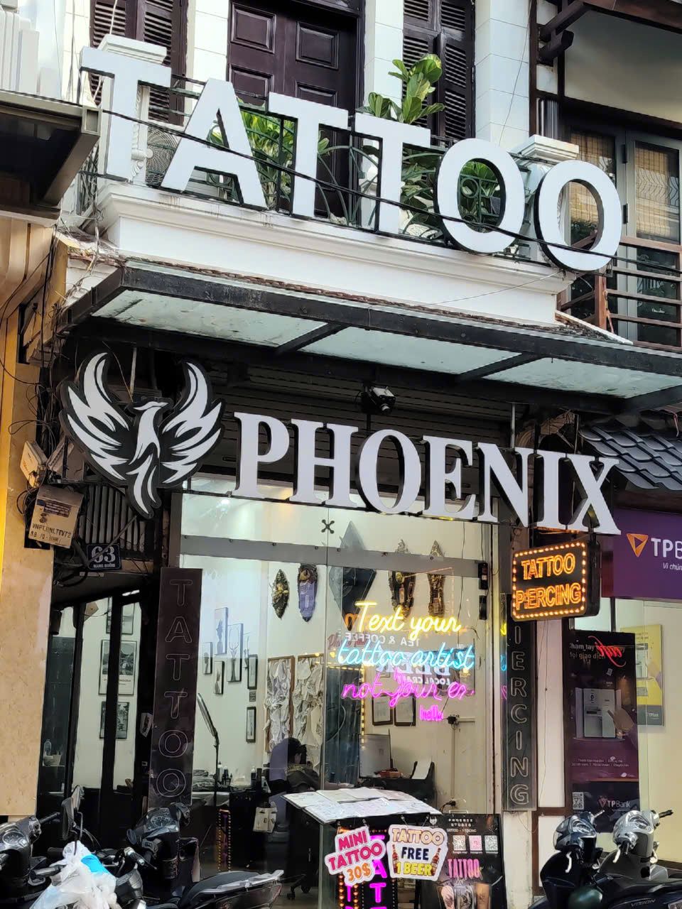 Un estudio de tatuajes llamado 'Phoenix', con un letrero llamativo y un anuncio de neón que dice 'TATTOO'.