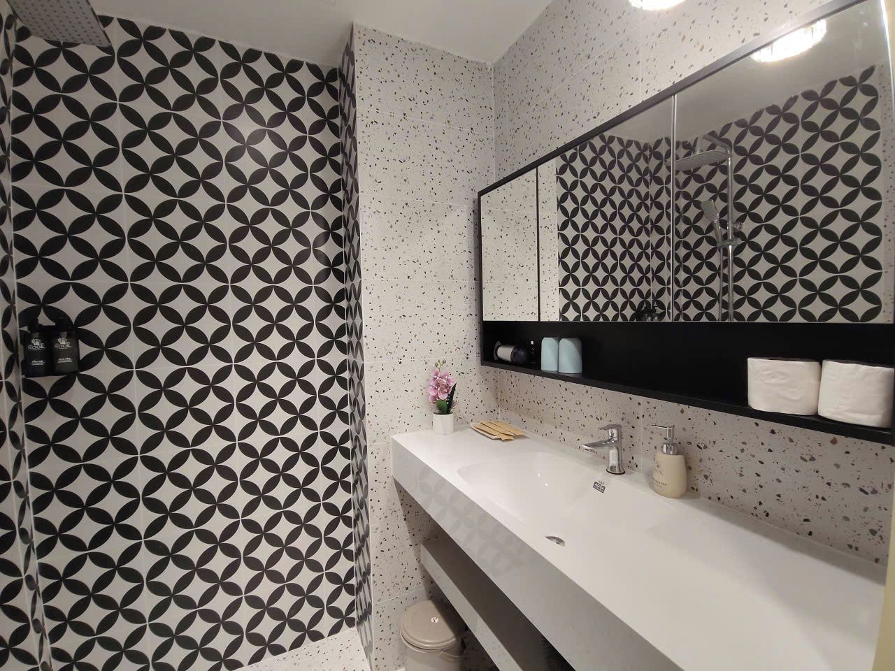 A bathroom with a geometric patterned shower curtain, a white sink with a mirror above it, and a shelf with toiletries.