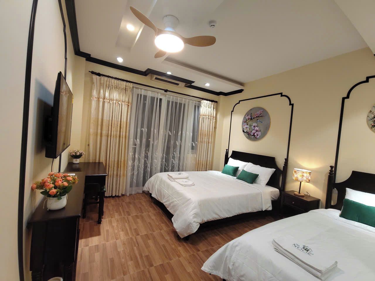 A hotel room with two beds, a television, a desk, and a ceiling fan.