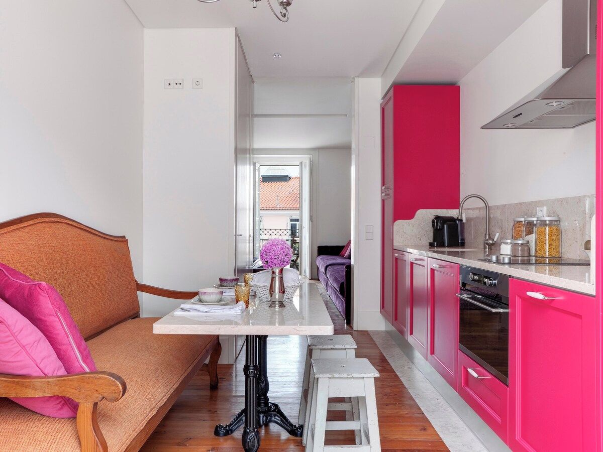 A modern kitchen with pink cabinets and a dining area with a wooden sofa and a small table.