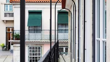 A narrow alleyway with a building featuring a tiled roof, a balcony with a metal railing, and a door with a green shutter.