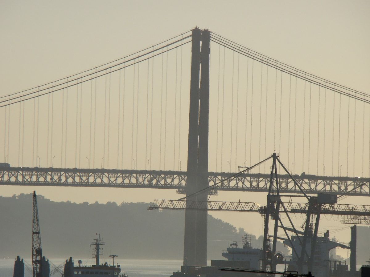 A large bridge with multiple cables and a prominent central tower, with industrial structures and water in the foreground.
