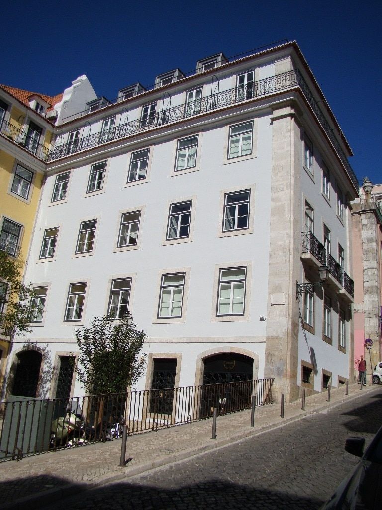 Un edificio de varios pisos con fachada blanca, numerosas ventanas y balcones.