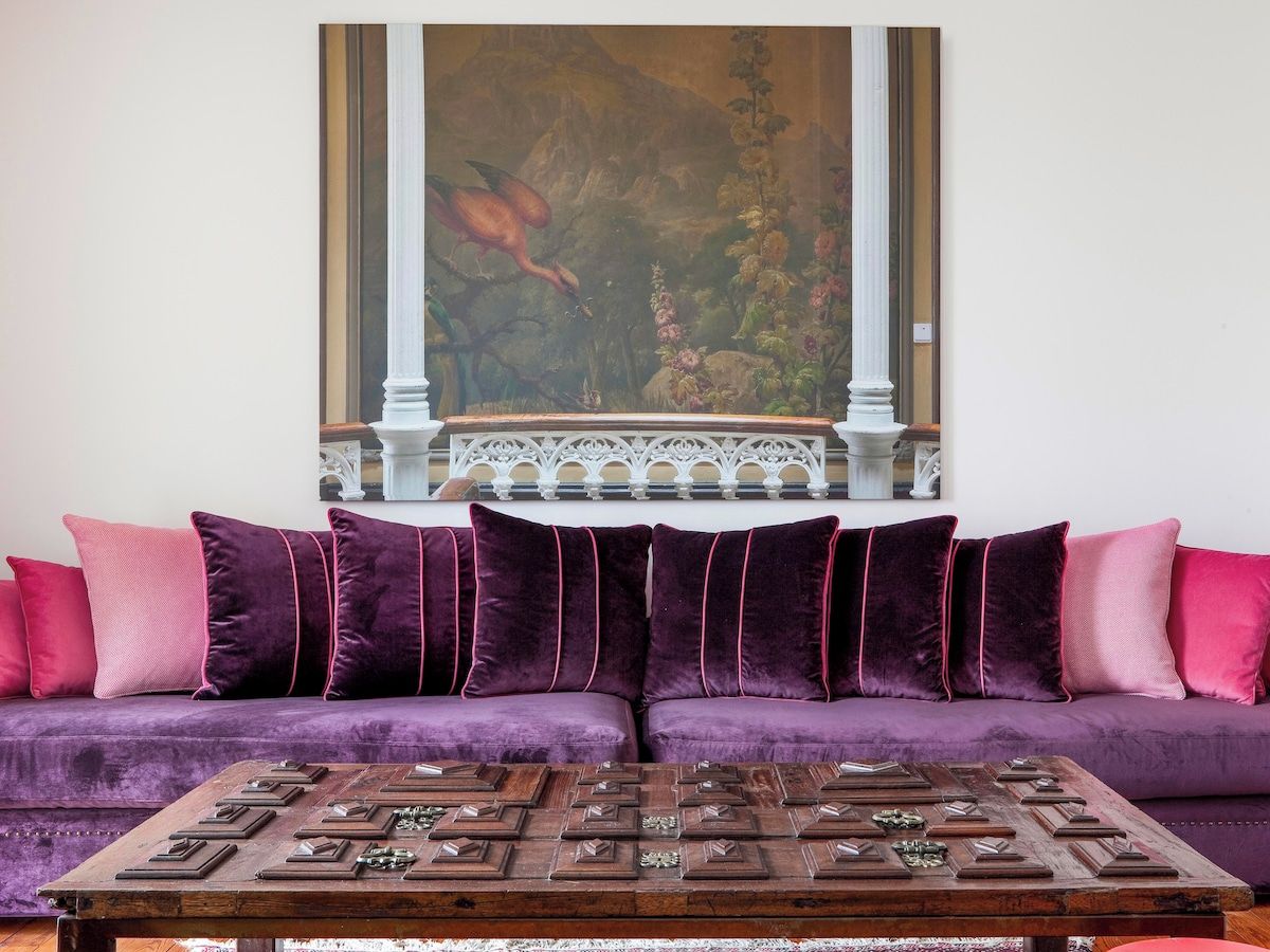 Una habitación con un sofá morado, una mesa de centro de madera con piezas de ajedrez y un cuadro sobre el sofá.