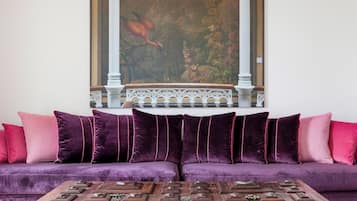 Una habitación con un sofá morado, una mesa de centro de madera con piezas de ajedrez y un cuadro sobre el sofá.